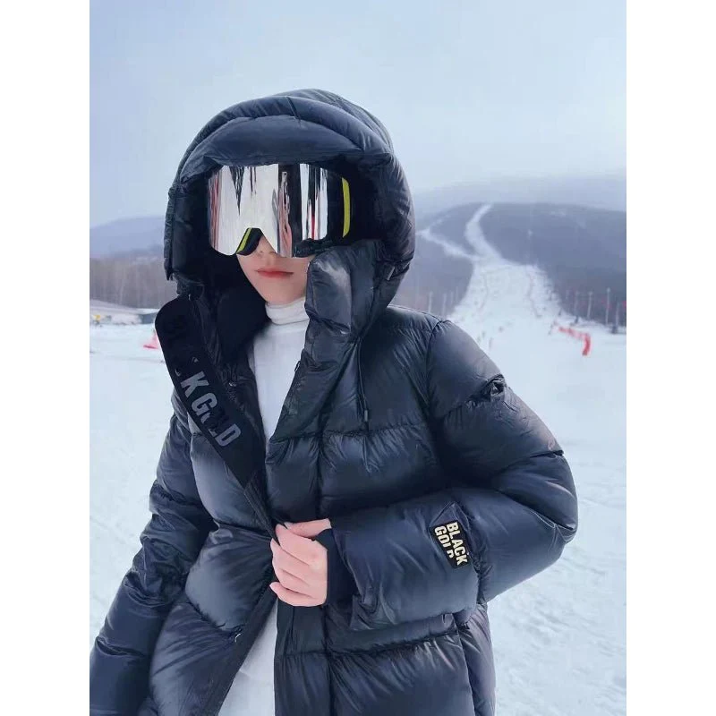 Person wearing a black puffer jacket and goggles on a snowy landscape