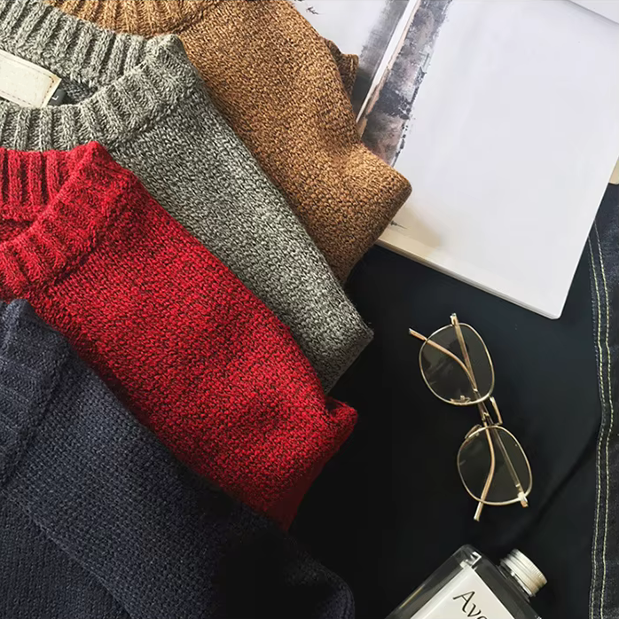 Stack of folded sweaters in red, gray, and brown with a pair of sunglasses on a dark surface.