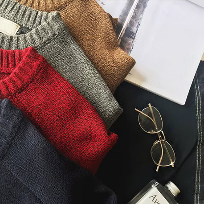 Stack of folded sweaters in red, gray, and brown with a pair of sunglasses on a dark surface.