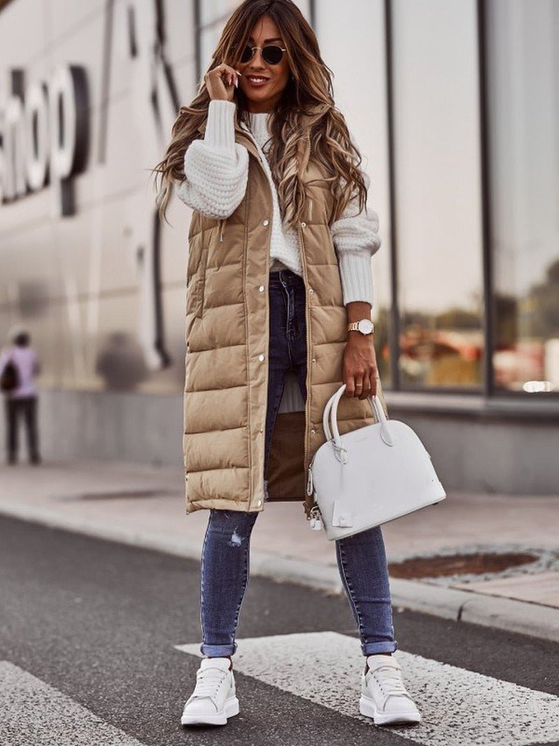 Woman wearing a long beige puffer vest with a white handbag on a city street.