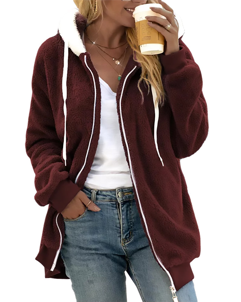 Person wearing a burgundy zip-up hoodie with a white shirt and blue jeans, holding a coffee cup.