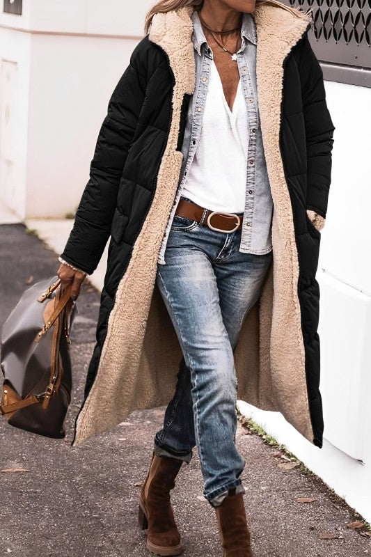 Person wearing a long black coat with beige lining, blue jeans, and brown boots on a street.