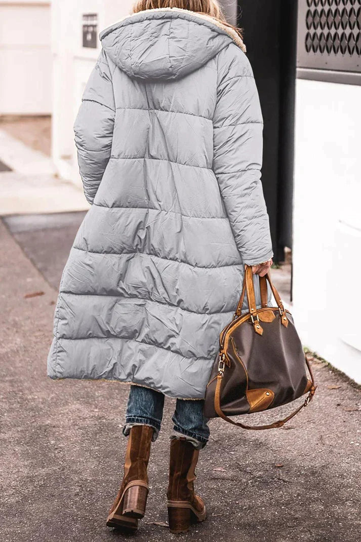 Person wearing a long light blue puffer coat with a hood, holding a brown leather handbag.