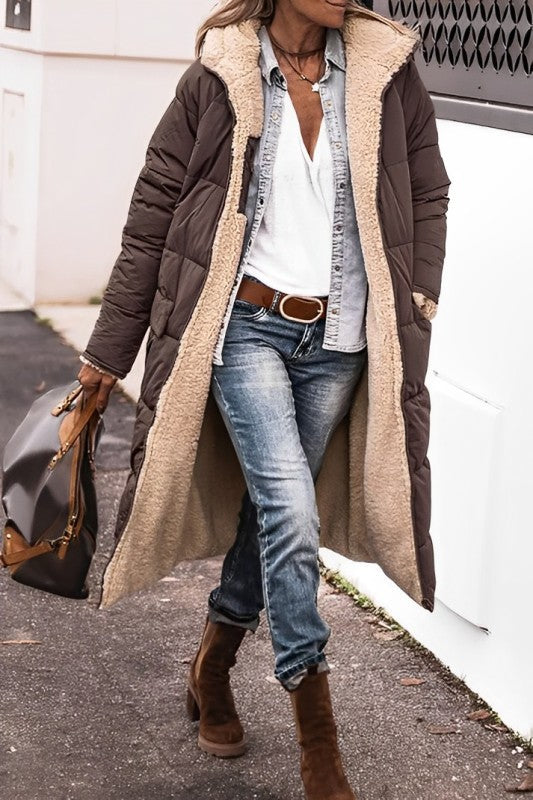 Person wearing a long brown coat with a beige fur-lined hood, blue jeans, and brown boots.