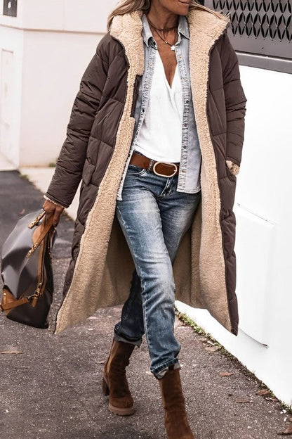 Person wearing a long brown coat with a beige fur-lined hood, blue jeans, and brown boots.