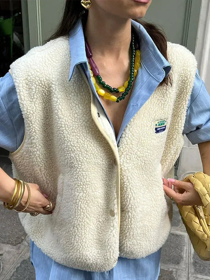 Person wearing a cream sherpa vest over a blue shirt with visible brand logo, holding a yellow bag.
