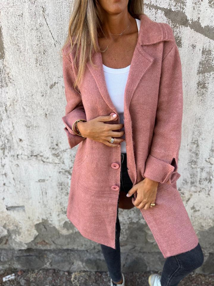 Person wearing a pink coat against a textured wall.