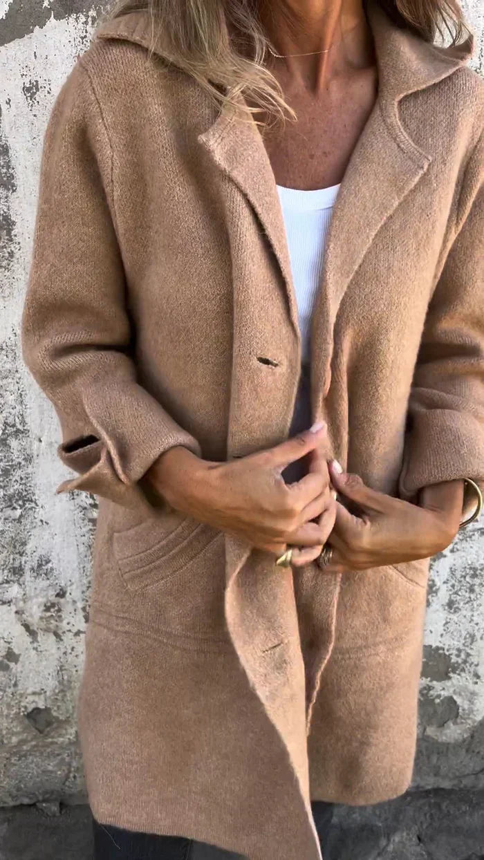 Person wearing a brown coat against a textured wall.
