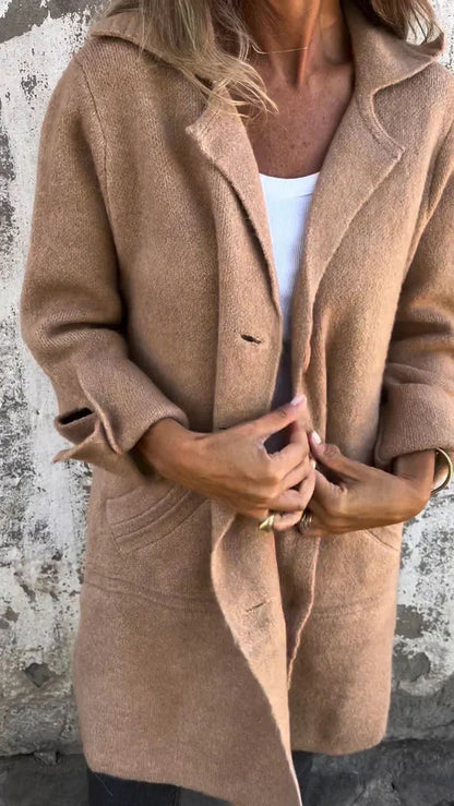 Person wearing a brown coat against a textured wall.