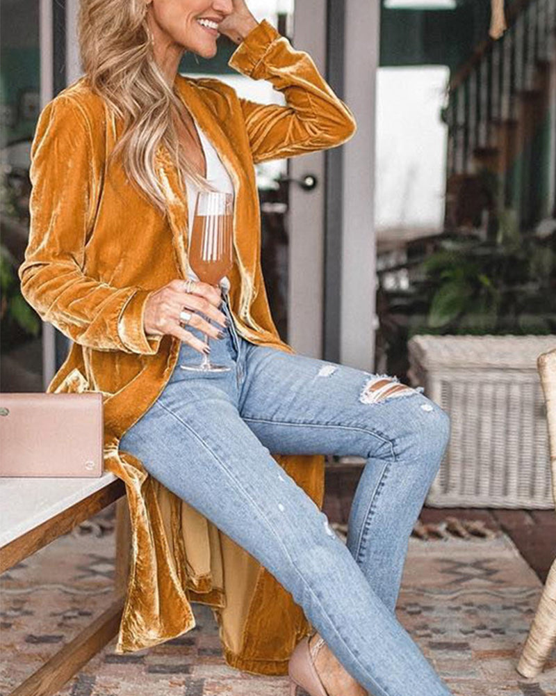 Woman wearing a mustard yellow velvet jacket and light blue jeans, sitting outdoors.