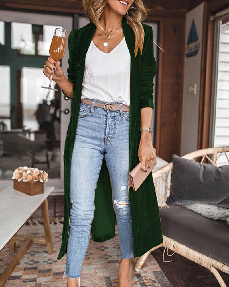Woman in a green cardigan, white top, and blue jeans holding a glass of champagne in a living room.