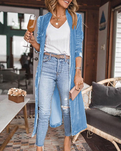 Woman in a casual outfit with a blue cardigan and jeans, holding a drink in a cozy indoor setting.
