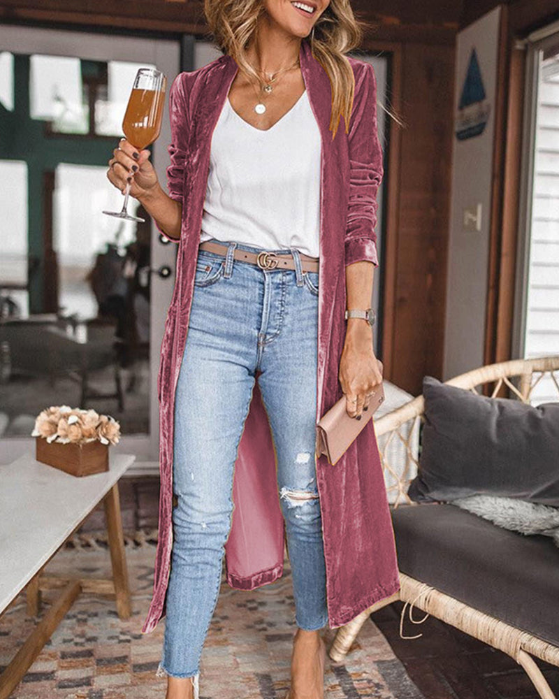Woman in a cozy living room wearing a long burgundy cardigan, white top, and blue jeans, holding a glass of champagne.