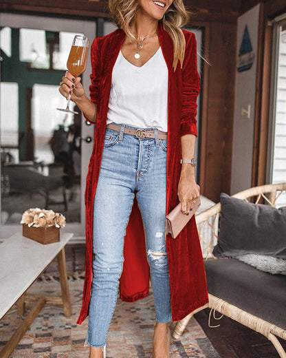 Woman in a red cardigan, white top, and blue jeans holding a drink in a casual setting.