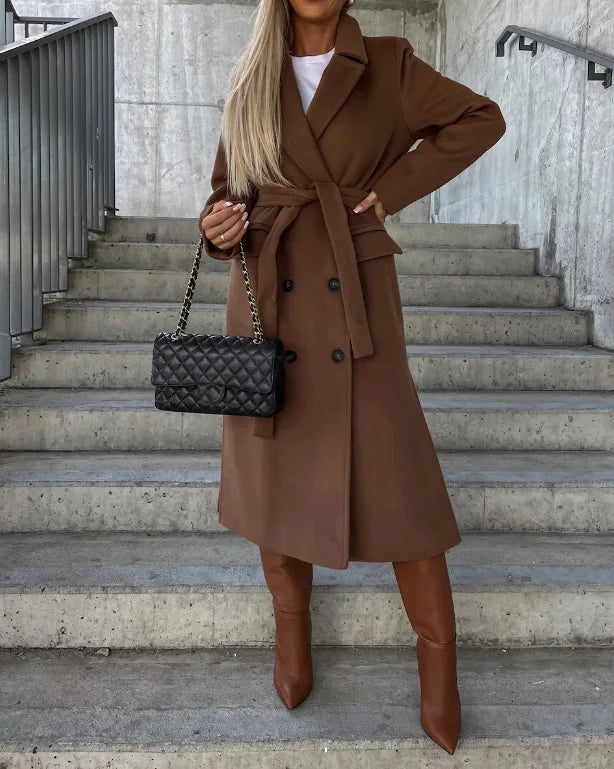 Person wearing a brown coat and boots, holding a black quilted handbag on steps.