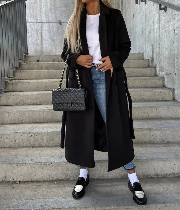 Person wearing a black coat and jeans with a black handbag on concrete steps.