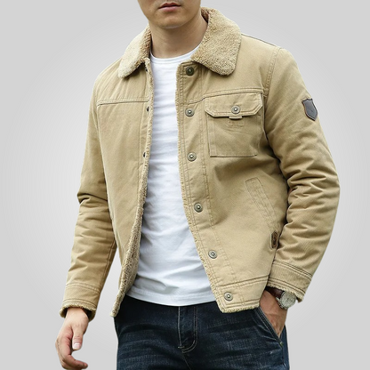 Man wearing a beige jacket with a white shirt and dark jeans on a gray background
