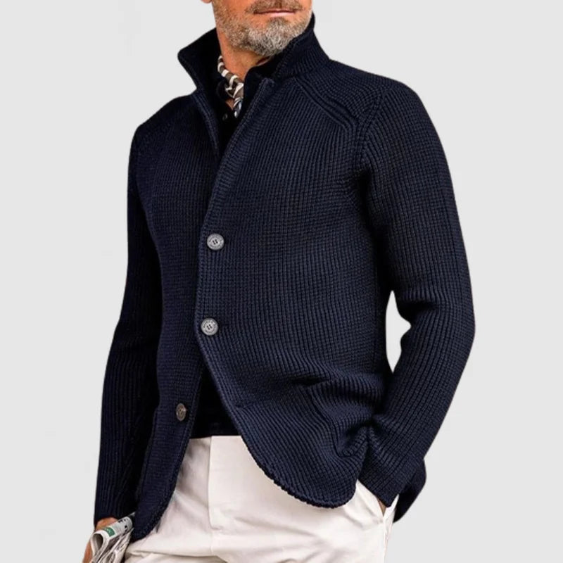 Man wearing a navy blue knitted cardigan over a white shirt on a light gray background