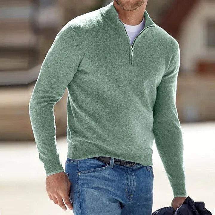 Person wearing a green sweater with a quarter zip and blue jeans in an outdoor setting