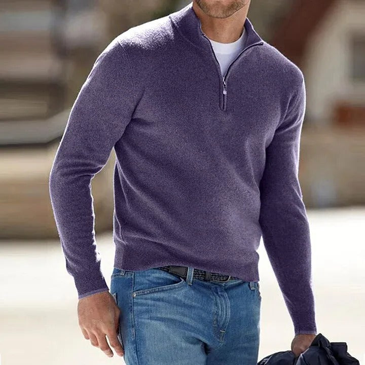 Man wearing a purple quarter-zip sweater and blue jeans outdoors.