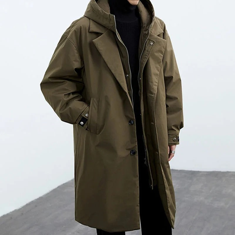 Long olive green coat worn by a person on a plain background