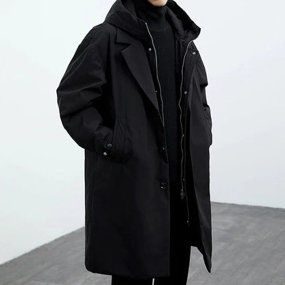 Person wearing a long black coat against a white background