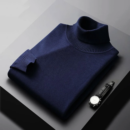 Folded navy blue turtleneck sweater on a gray surface with a watch beside it.