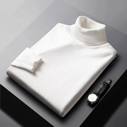 Folded white turtleneck sweater on a gray surface with a black watch.