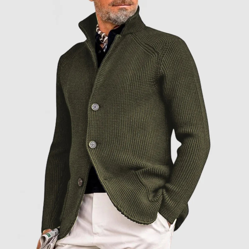 Man wearing a green knitted cardigan over a black shirt on a light gray background