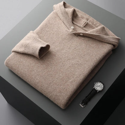 Folded beige sweater on a dark surface with a watch beside it