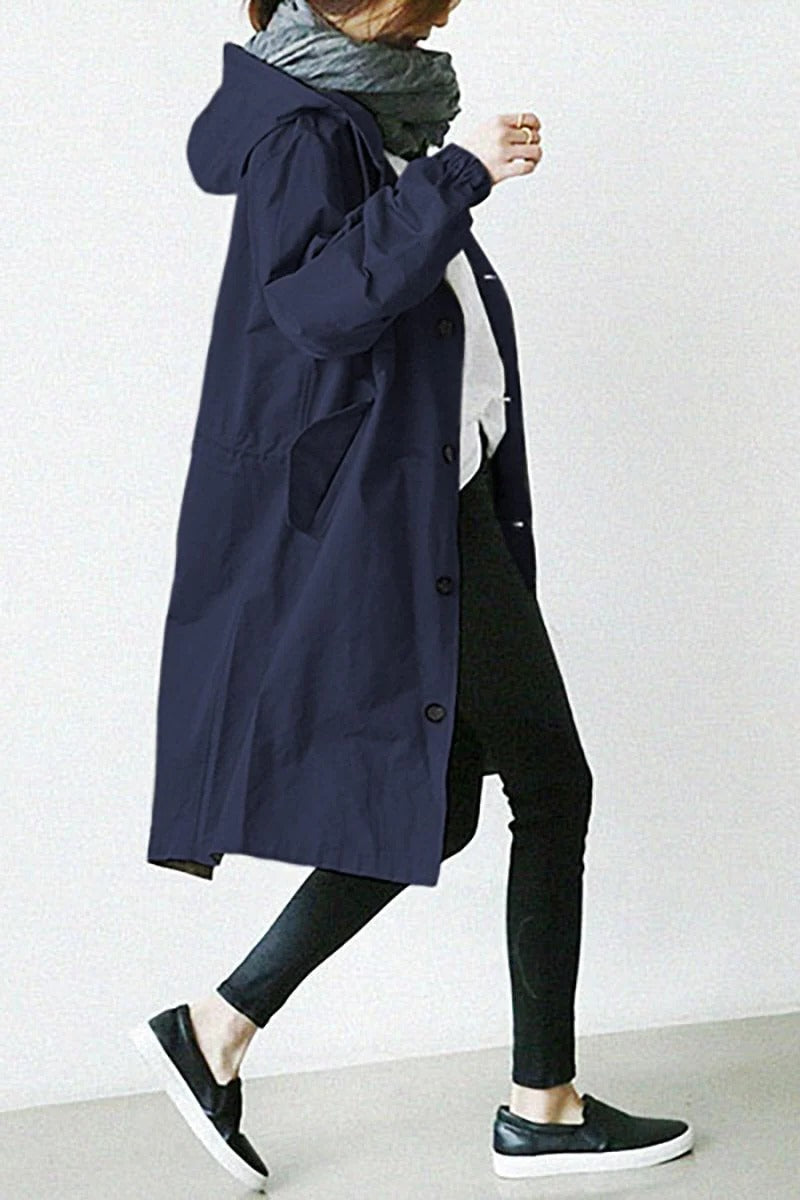 Person wearing a long navy coat with a plain background