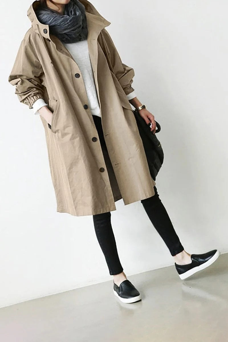 Person wearing a beige trench coat over a white shirt with black pants and shoes on a plain background