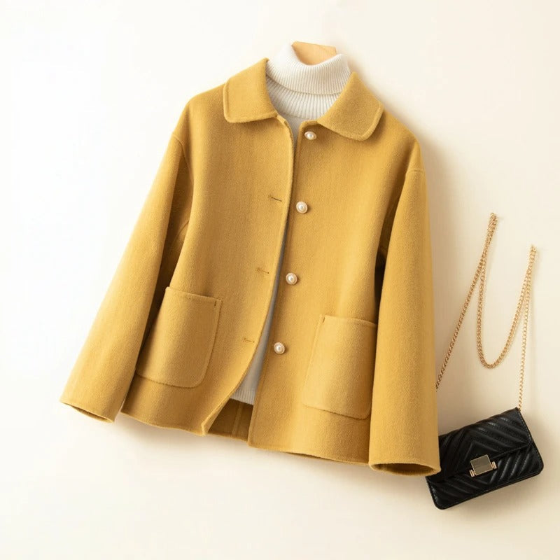 Mustard yellow coat with a white turtleneck and black handbag on a light beige background