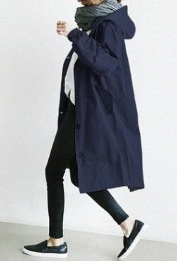 Person wearing a long navy coat with a plain background