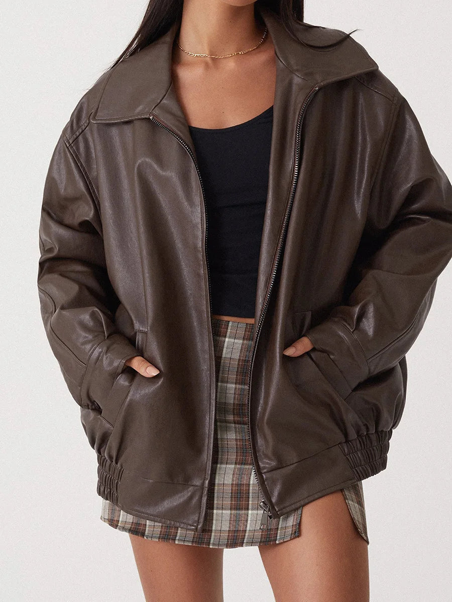 Person wearing a brown leather jacket over a black top and plaid skirt on a white background