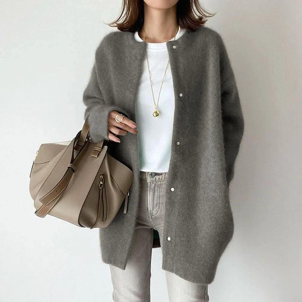 Person wearing a gray cardigan, white shirt, and jeans, holding a beige handbag against a plain background