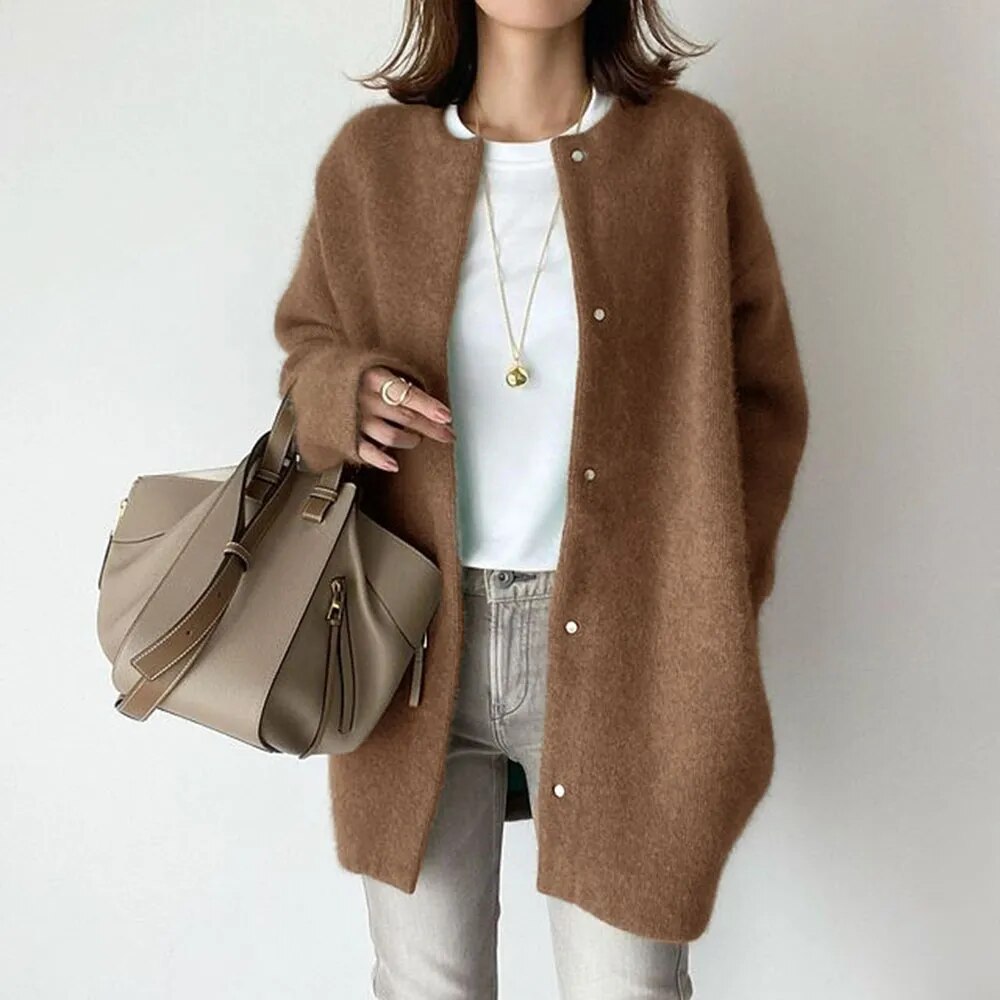 Person wearing a brown cardigan holding a beige handbag on a plain background