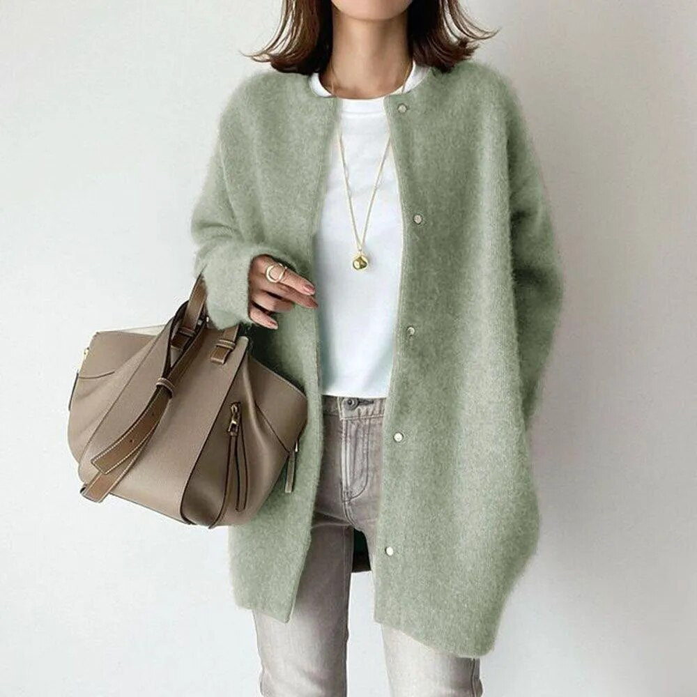 Person wearing a light green cardigan holding a beige handbag on a plain background