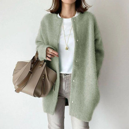 Person wearing a light green cardigan holding a beige handbag on a plain background